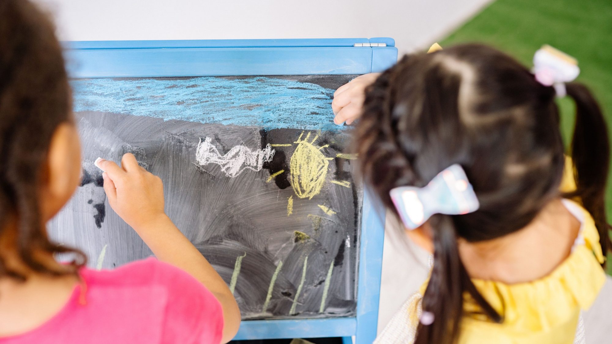 Dos niñas dibujan con tizas de colores en una pizarra durante una actividad de aula