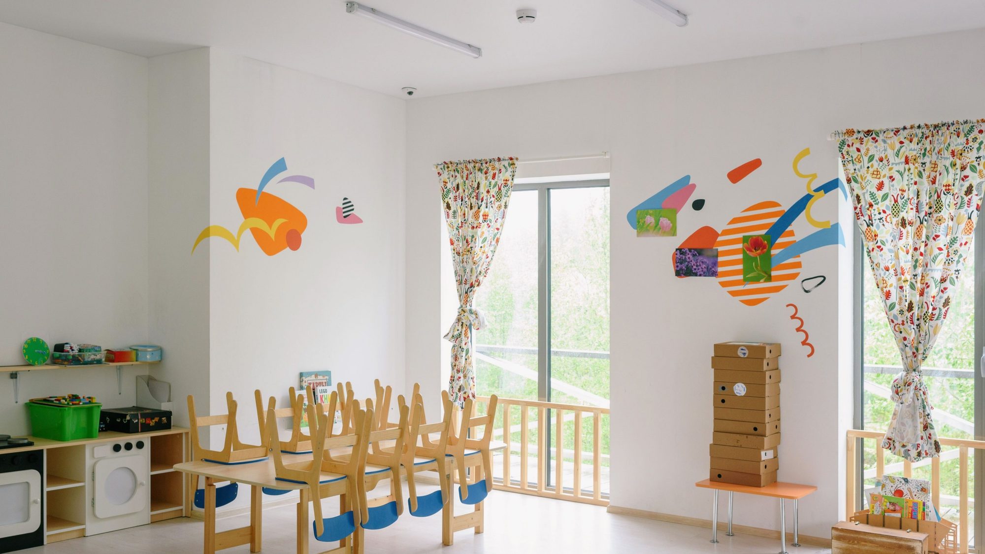 Aula de escuela infantil con sillas de madera, mesas bajas y murales de colores en la pared